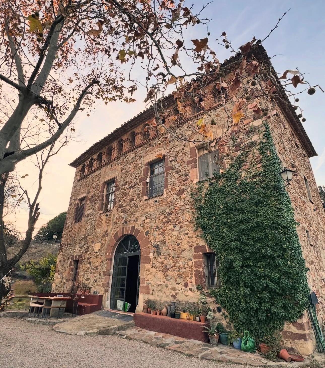 A stone retreat house covered in ivy, with an arched doorway, autumn leaves and potted plants at the entrance