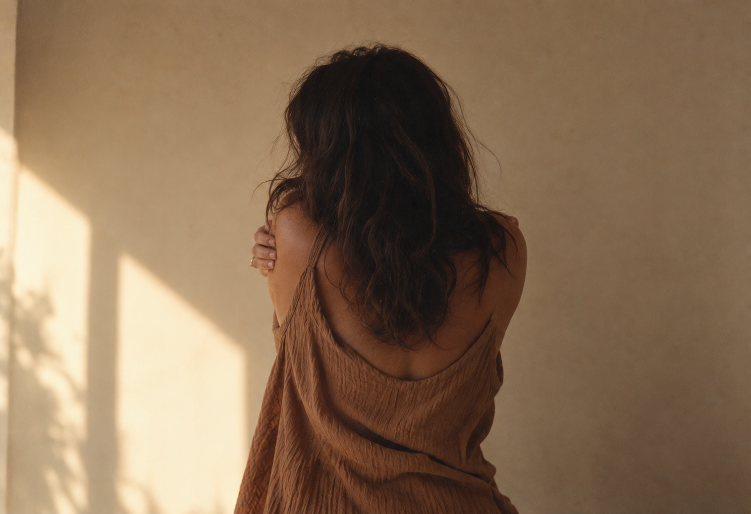 A woman seen from behind in warm afternoon light, holding her shoulder